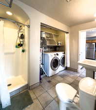 Bathroom with washer and dryer, a textured ceiling, a shower stall, and light tile patterned floors
