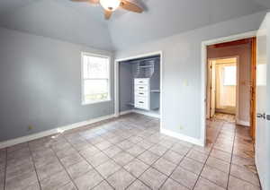 Unfurnished bedroom with a closet, light tile patterned floors, lofted ceiling, and ceiling fan