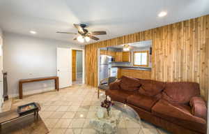Living room featuring wooden walls, recessed lighting, light tile patterned flooring, and a ceiling fan