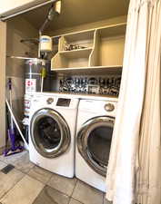 Laundry area featuring strapped water heater, light tile patterned floors, and washer and dryer