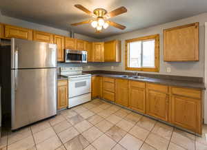 Kitchen featuring stainless steel appliances, a ceiling fan, dark countertops, wood finish cabinetry, and light tile patterned floors