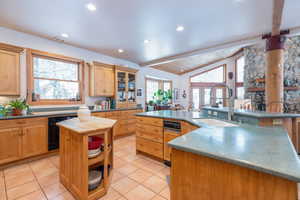 Kitchen with vaulted ceiling with beams, glass insert cabinets, black oven, light tile patterned floors, and light wood finish cabinets