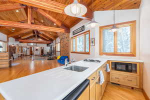 Kitchen with light countertops, light wood finished floors, a high wooden beamed ceiling, open floor plan, and black microwave