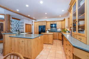 Kitchen with glass fronted cabinets, light wood finish cabinets, black appliances, light tile patterned floors, and recessed lighting