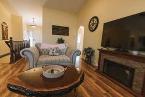 Living area with wood finished floors, arched walkways, a fireplace, and vaulted ceiling