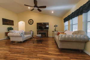 Living room featuring a ceiling fan, lofted ceiling, wood finished floors, arched walkways, and a brick fireplace
