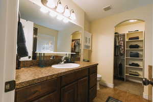 Full bathroom featuring vanity, dark tile patterned flooring, and a walk in closet