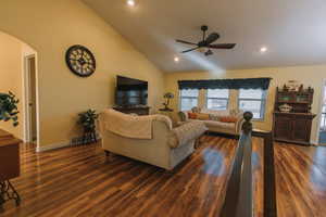Living room featuring arched walkways, vaulted ceiling, dark wood-type flooring, recessed lighting, and a ceiling fan