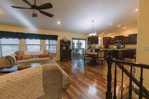 Living room with vaulted ceiling, hanging lights, dark wood-type flooring, and a ceiling fan