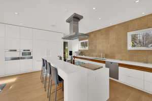 Kitchen with modern cabinets, a breakfast bar, island exhaust hood, integrated Miele appliances, and light wood-style floors