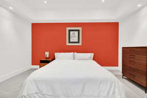 Bedroom with light colored carpet, a raised ceiling, and recessed lighting
