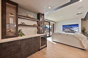Bar featuring dark wood finish cabinets, light countertops, glass fronted cabinets, light wood-type flooring, and beverage cooler