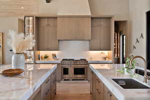 Kitchen featuring double oven range, light stone counters, and light wood-style floors