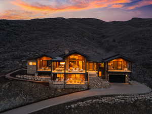 Back of property at dusk with a chimney, driveway, a garage, and stone siding