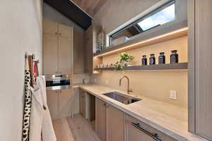 Kitchen with light stone counters, open shelves, light wood finish cabinets, stainless steel oven, and lofted ceiling