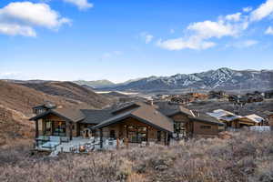 Back of property with a patio, a mountain view, a shingled roof, and stone siding
