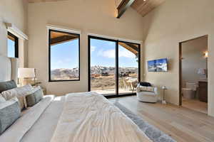 Bedroom with light wood-type flooring, vaulted ceiling, access to exterior, and connected bathroom