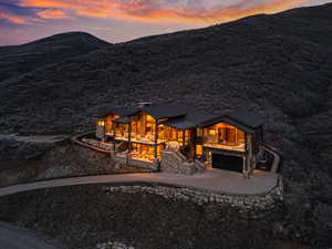 Back of property at dusk with stone siding, driveway, a garage, a mountain view, and a porch