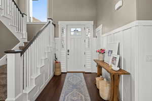 Foyer entrance featuring dark wood-style floors, a wainscoted wall, a decorative wall, and a high ceiling