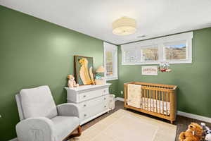 Bedroom featuring a nursery area, carpet floors, and a textured ceiling