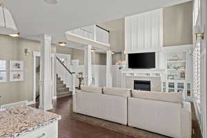 Living area featuring dark wood-style flooring, a glass covered fireplace, ornate columns, and plenty of natural light