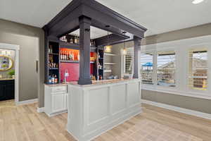 Indoor wet bar with open shelves, light wood-style flooring, light stone counters, decorative light fixtures, and white cabinets
