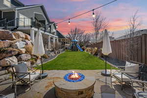 Fenced backyard with a playground, a patio area, and an outdoor fire pit