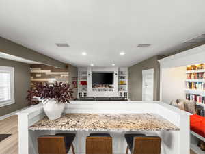 Bar area featuring light wood-type flooring, light stone counters, and recessed lighting