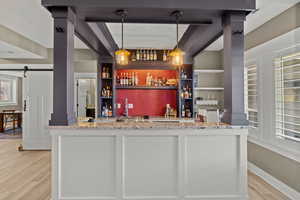 Indoor wet bar with light wood-type flooring, a barn door, open shelves, built in features, and pendant lighting