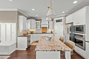 Kitchen featuring a breakfast bar, white cabinetry, dark stone countertops, stainless steel appliances, and glass fronted cabinets