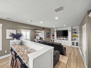 Kitchen with light wood-style flooring, light countertops, a breakfast bar area, built in shelves, and recessed lighting