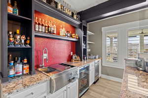 Indoor wet bar with open shelves, wine cooler, light wood-style flooring, and light stone countertops