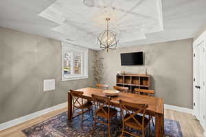 Dining area with light wood-style floors, hanging lights, a raised ceiling, and a textured ceiling