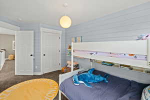 Bedroom with carpet flooring, a closet, and wood walls