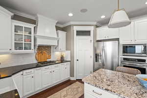 Kitchen with white cabinets, stainless steel appliances, dark stone countertops, crown molding, and decorative backsplash