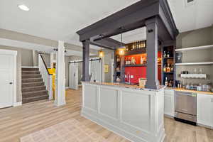 Indoor wet bar with hanging light fixtures, open shelves, light wood-style flooring, and stainless steel dishwasher