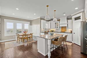 Kitchen featuring white cabinets, glass fronted cabinets, dark stone countertops, decorative light fixtures, and a kitchen island