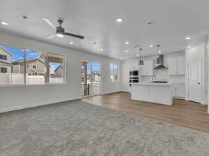 Kitchen with open floor plan, white cabinetry, a textured ceiling, an island with sink, and light colored carpet