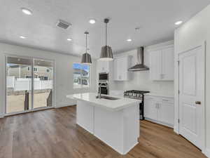 Kitchen with stainless steel appliances, a kitchen island with sink, white cabinets, hanging light fixtures, and a textured ceiling