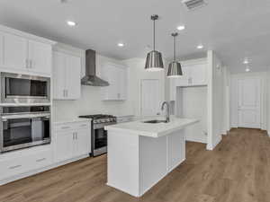Kitchen featuring stainless steel appliances, a kitchen island with sink, white cabinets, light wood-type flooring, and a textured ceiling