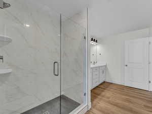 Bathroom featuring a marble finish shower, light wood-style floors, and vanity