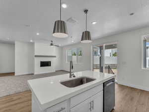 Kitchen with a fireplace, a textured ceiling, white cabinets, a kitchen island with sink, and pendant lighting
