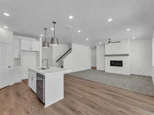 Kitchen with white cabinets, a center island with sink, a fireplace, open floor plan, and decorative light fixtures