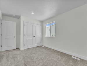 Unfurnished bedroom featuring light carpet, a closet, and a textured ceiling
