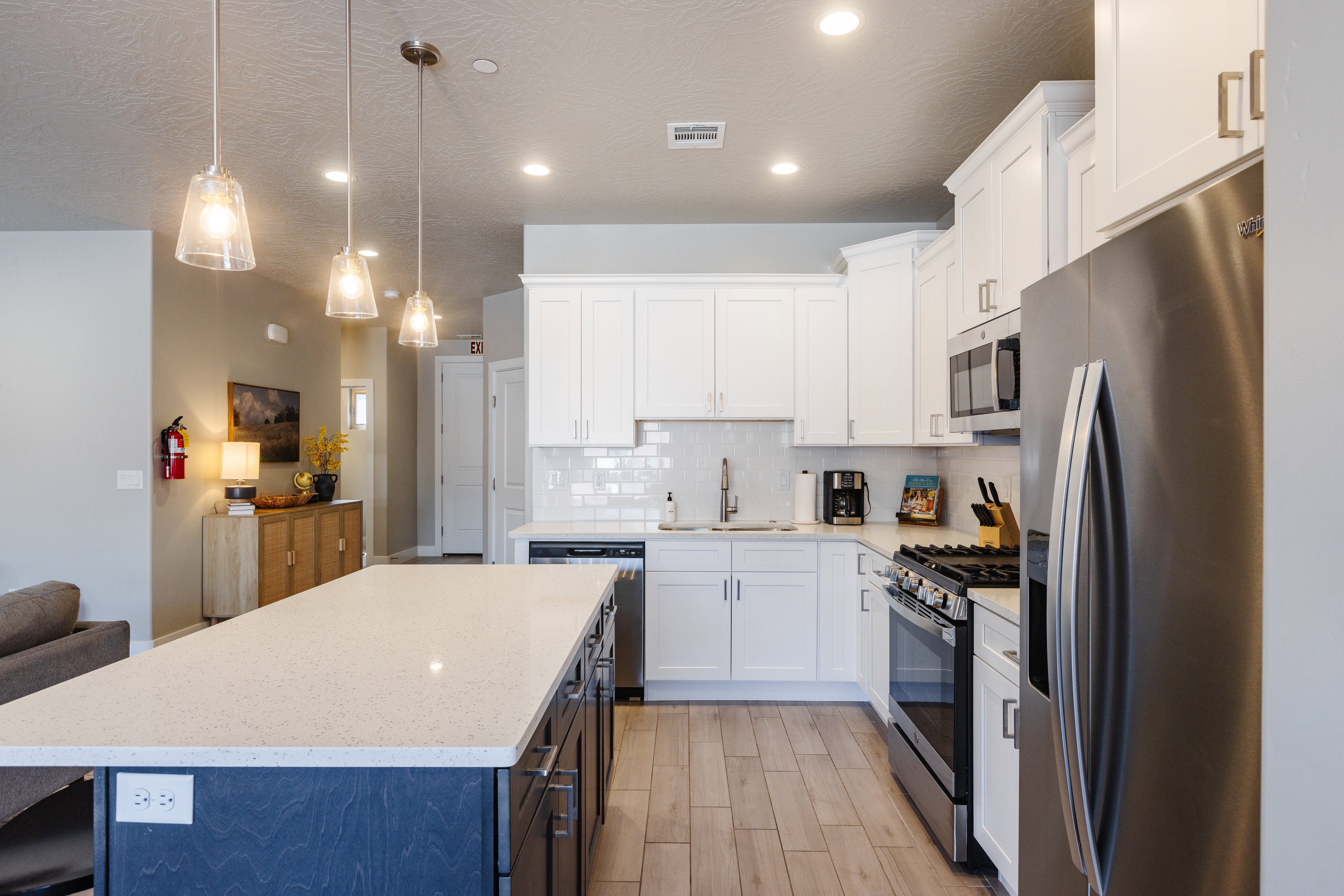 Two tone kitchen with stainless steel appliances, a center island, light stone countertops, open floor plan, and two tone cabinets