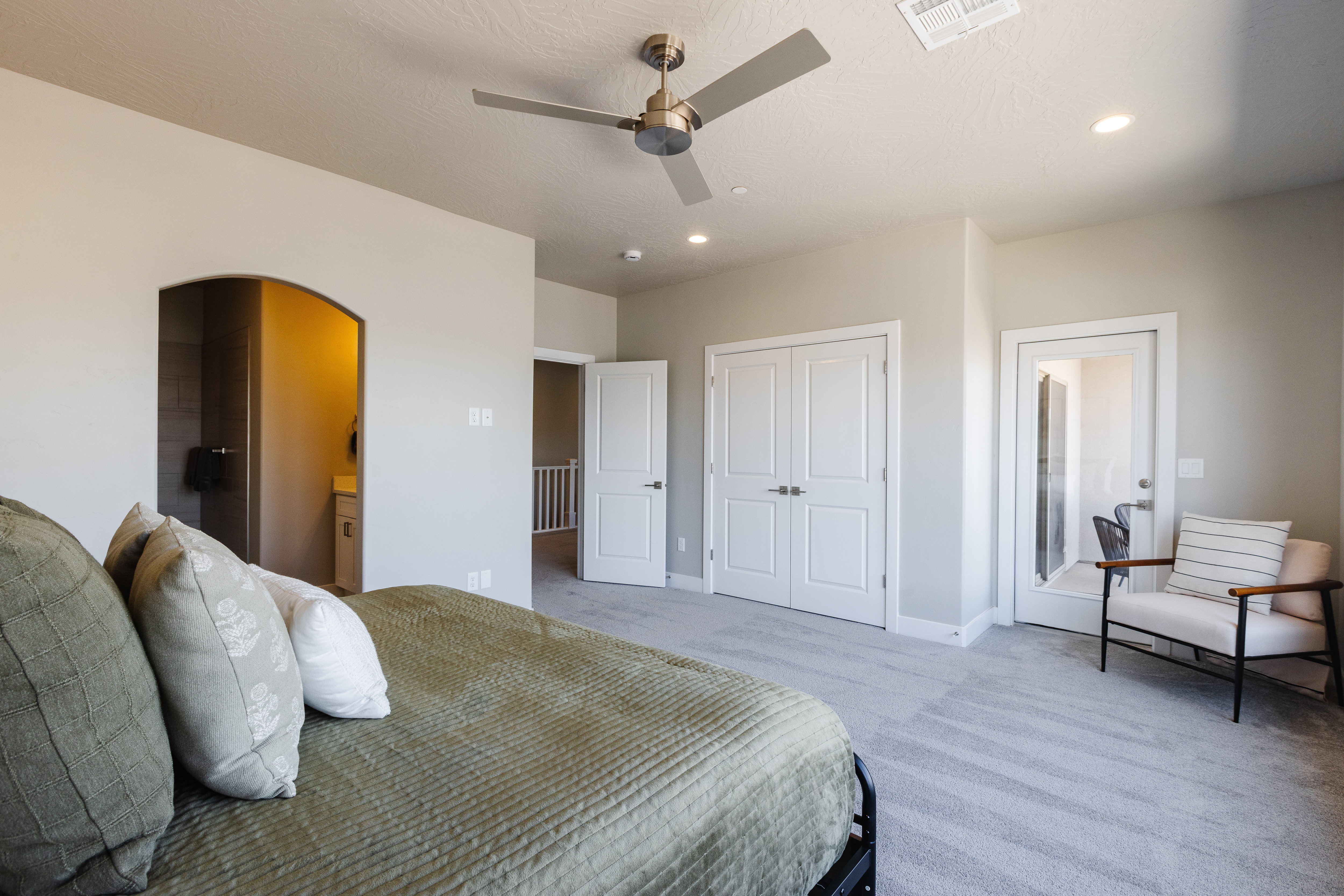 Bedroom with light carpet, ensuite bath, a ceiling fan, arched walkways, and a closet
