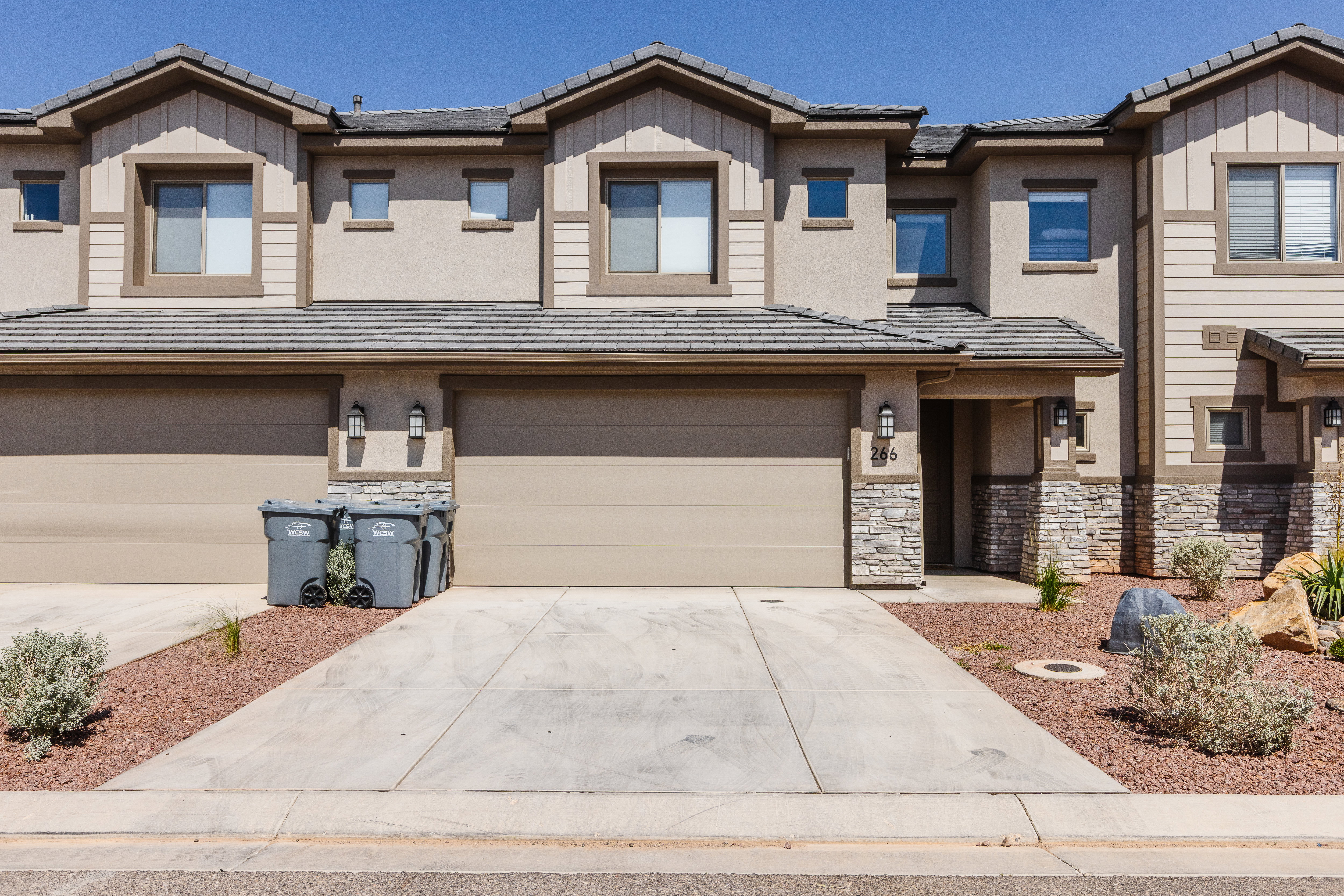 View of front of home with a tiled roof, board and batten siding, driveway, a garage, and stone siding