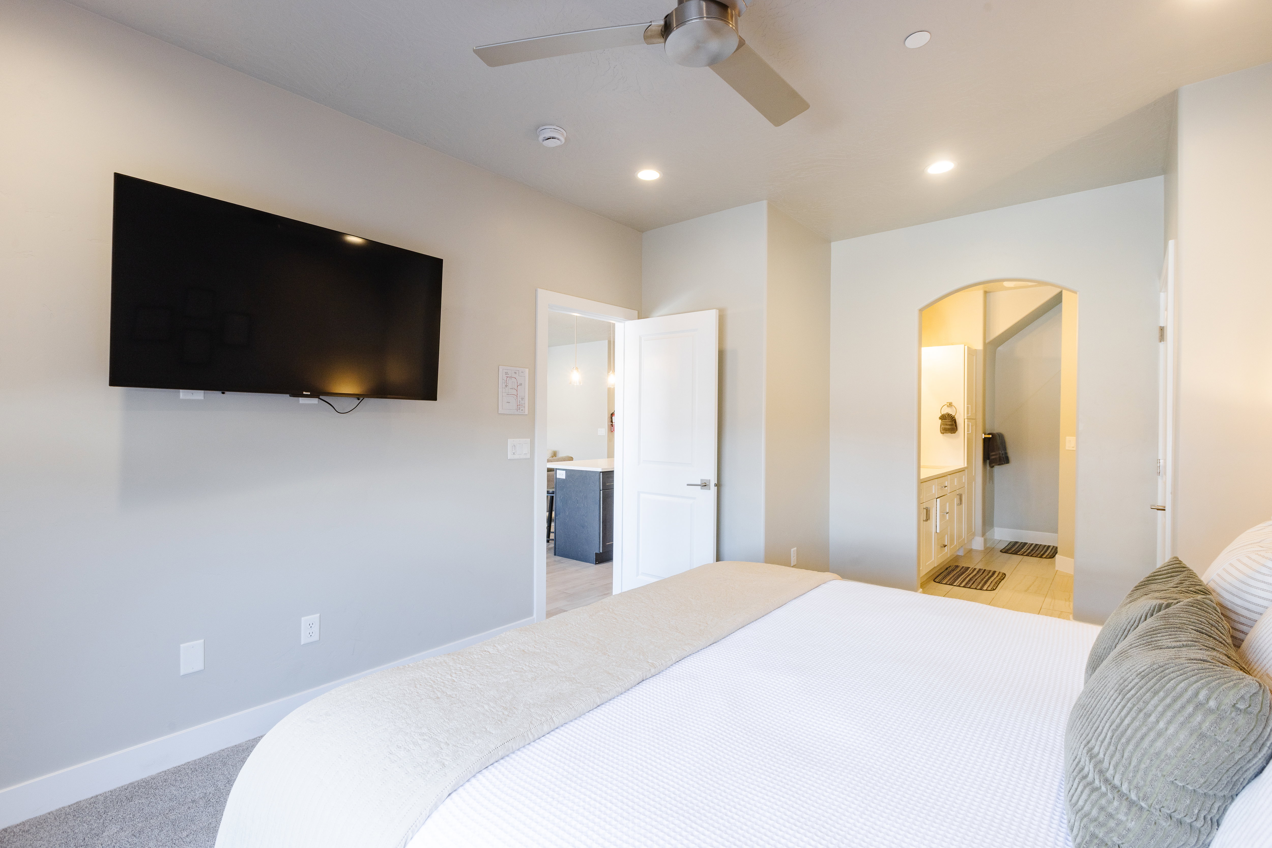 Bedroom with arched walkways, light colored carpet, ceiling fan, connected bathroom, and recessed lighting