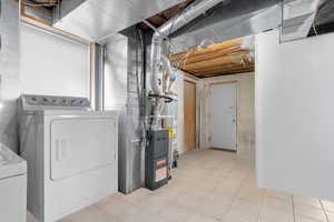 Unfinished below grade area featuring heating unit, water heater, and washer and clothes dryer