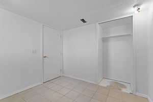 Unfurnished bedroom featuring a textured ceiling, a closet, and light tile patterned floors
